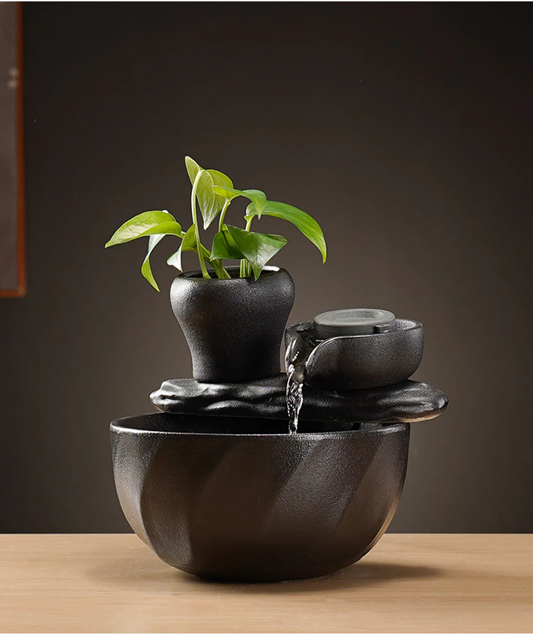 Black ceramic tabletop fountain with green plant and water flowing from a round bowl